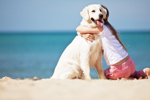 A girl hugging her dog on the beach.