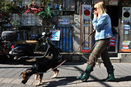 Mujer paseando a su perro en la calle mientras fuma.
