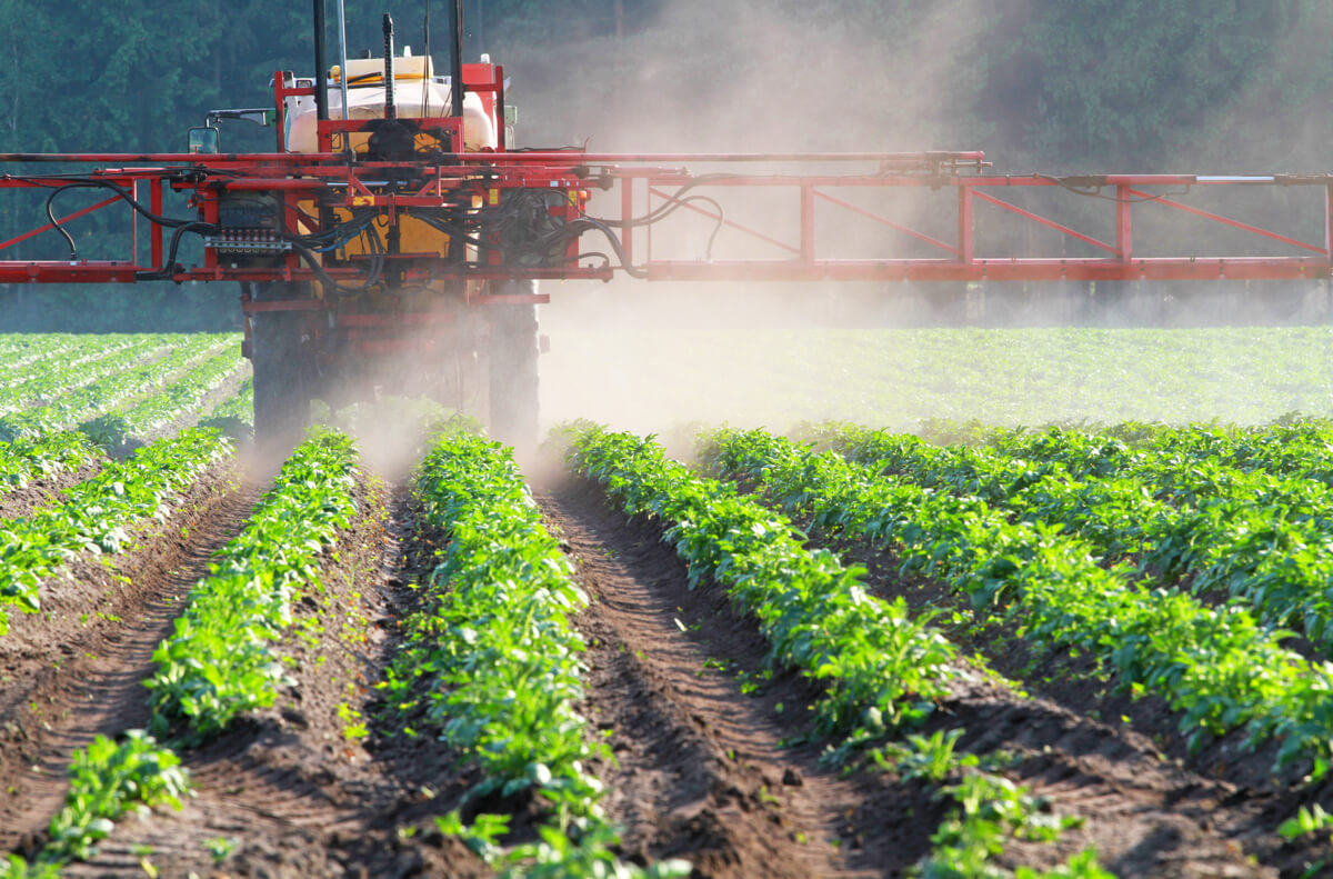 Un tractor con plaguicida rociando un cultivo.