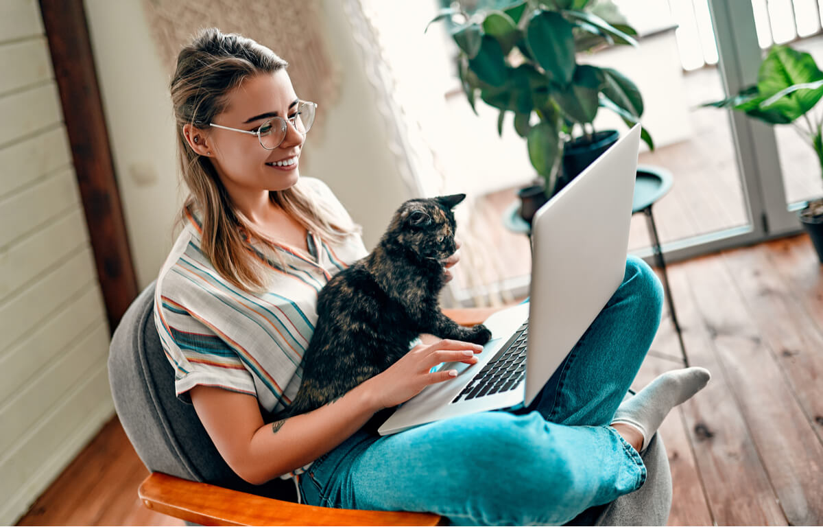 Una mujer mira a un ordenador con su gato.