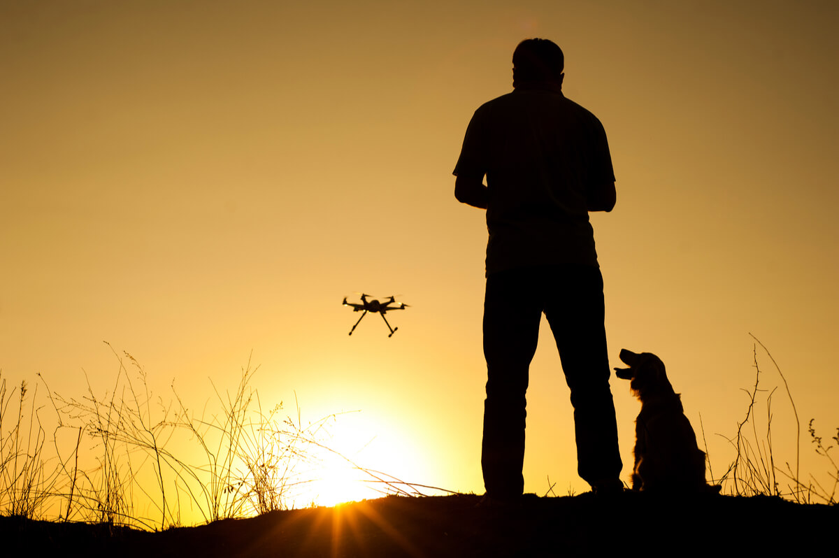 Una persona pilota un dron en compañía de un perro.