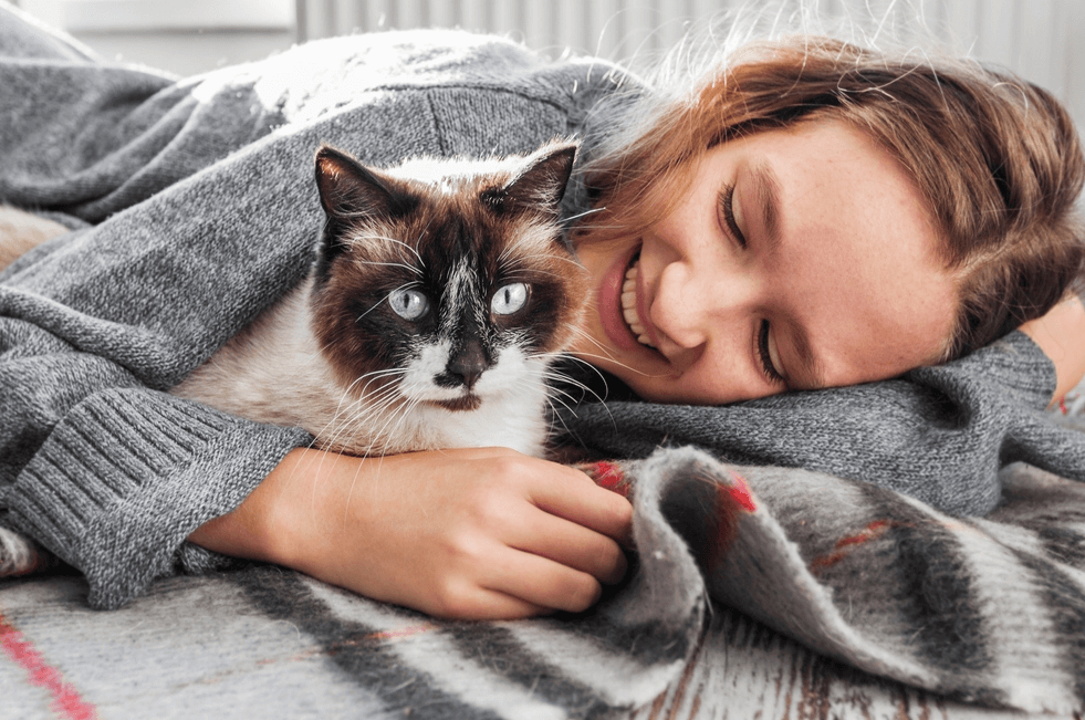 A young woman lying down and hugging a brown and white cat.